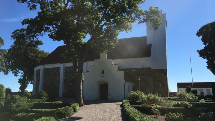 Et hvidt historisk hus med tårn og mursten, omgivet af grønne træer og buske