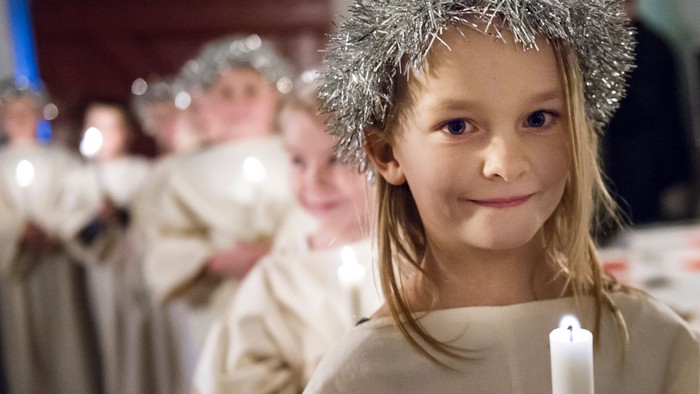 Unge pige med festligt gloriehovedstykke, der holder et lys under en ceremoniel procession.