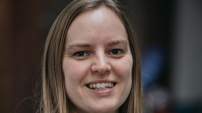 En smilende kvinde med glat brunt hår iført en grå sweater.