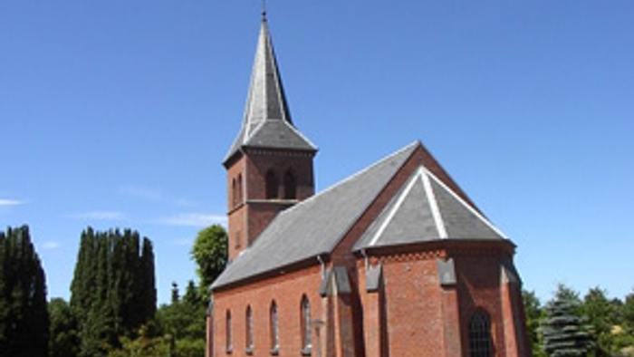 En charmerende rødstenskirke med et højt spir mod en klar blå himmel.