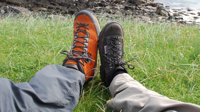 Beine mit Wanderschuhen auf einer grünen Wiese mit Felsen am Meer