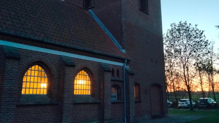 En murstenet kirke med spids tak og lysende vinduer ved solnedgang