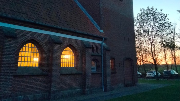 En murstenet kirke med spids tak og lysende vinduer ved solnedgang