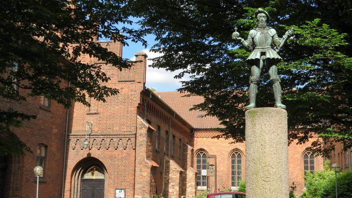 En statue foran et rødt murstensbygning med bil i forgrunden