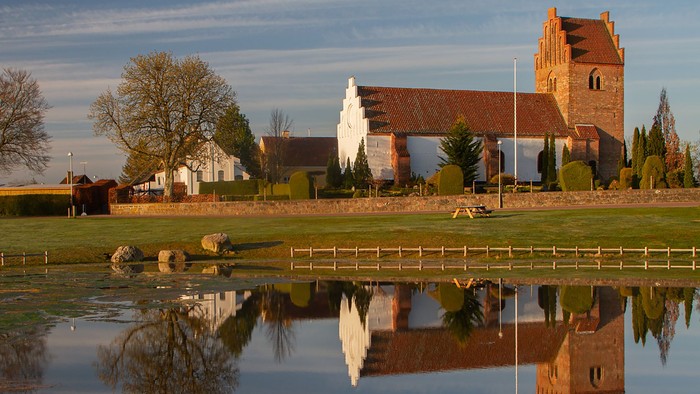 En rodfangst med en rød murstenskirke og træer, der reflekterer i en sø
