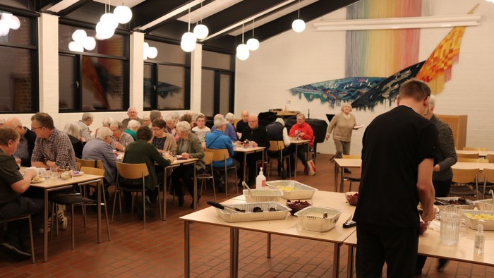 Gruppe af mennesker, der spiser ved borde på en restaurant.