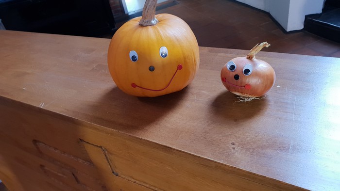 Süßer Kürbis und Zwiebel mit aufgemalten Gesichtern auf einer Holzoberfläche.