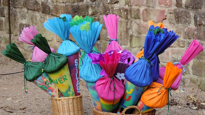 Bunte, blumengefüllte Taschen in geflochtenen Körben vor einem Ziegelwand-Hintergrund arrangiert.