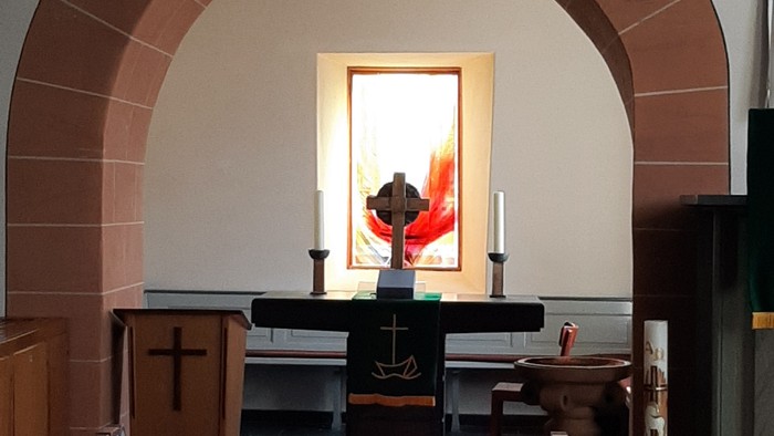 Idyllischer Kirchenaltarbereich mit hölzernen Kirchenbänken, Kerzen und einem Kruzifix, eingerahmt von einer gewölbten Steinmauer.