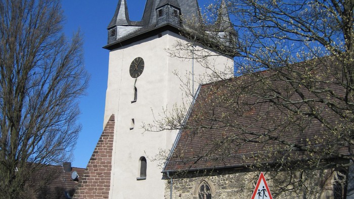 Außenansicht der evangelischen Kirche in Dörnberg. Helles Kirchenschiff aus Naturstein mit rotem Dach und hohem Turm.