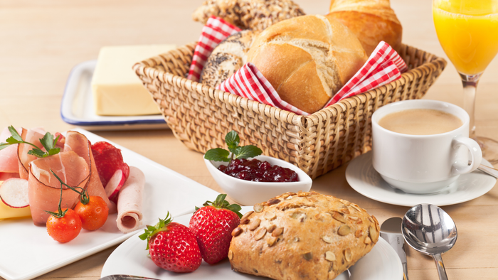 Frühstückskorb mit Brötchen, Butter, Aufschnitt, Marmelade, eine Tasse Kaffee, ein Glas Orangensaft