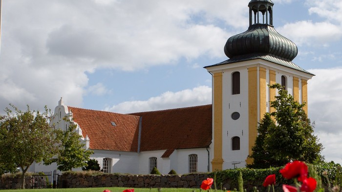 En smuk kirke med gul og hvid farve, en sort kuppel og røde blomster i forgrunden
