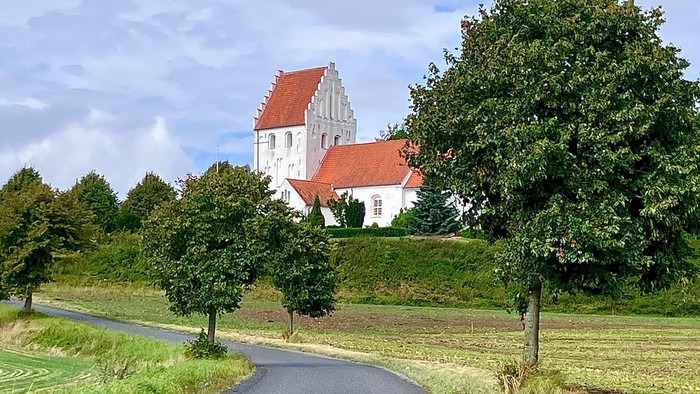 Malerværdig landevej, der fører til en charmerende hvid kirke med rødt tag.