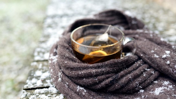 Eine dampfende Tasse Tee steht auf einem frostigen, gestrickten Schal im Freien.