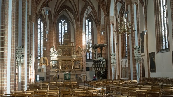 Großes Kathedraleninneres mit prunkvollem Altar, hohen Buntglasfenstern und hölzernen Kirchenbänken.