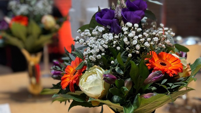 Livligt buket i en gul vase med lilla blomster, grønt og orange blomster på et træbord.
