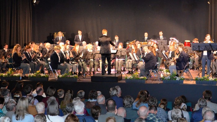 Ein Orchester spielt auf einer Bühne vor einem großen Publikum