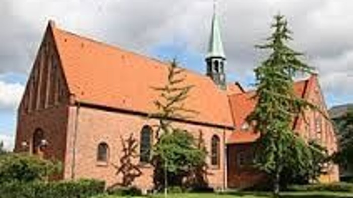 En lille rød kirke med spiret og træer foran