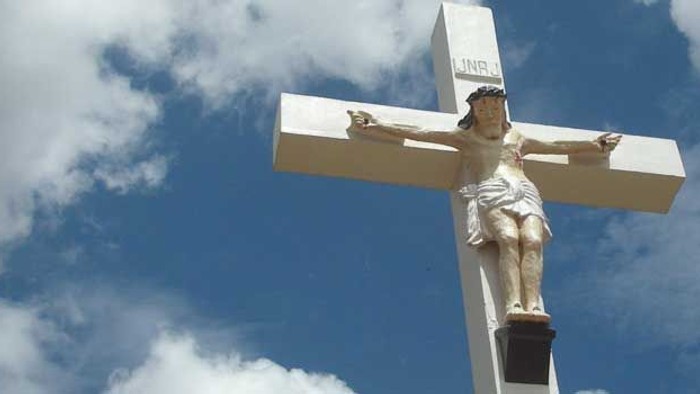 En stor hvid kors med en Jesus-statue i en blå himmel med skyer.