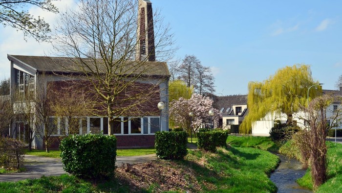 Ein modernes Gebäude mit Glasfront und Turm, umgeben von blühenden Bäumen und einem gepflegten Garten.
