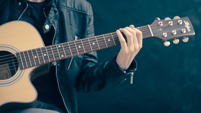 Eine Person spielt eine akustische Gitarre mit den Fingern auf dem Griffbrett positioniert.