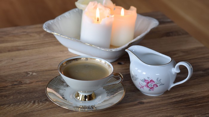 Ein Holztisch mit einer Teetasse, Milchkännchen und brennenden Kerzen in einer Schale