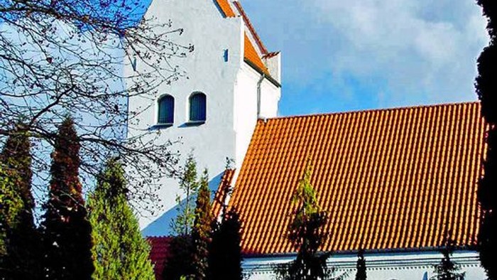 Et hvidt kirkebygning med røde tag og tre.