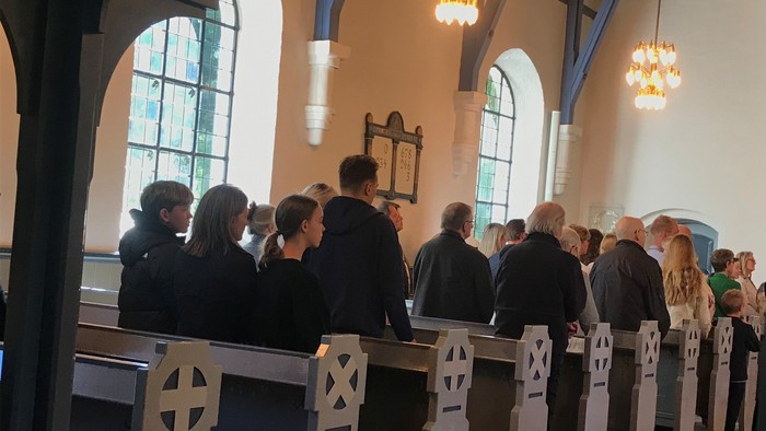 En gruppe af mennesker står i en kirke og deltager i en ceremoni.