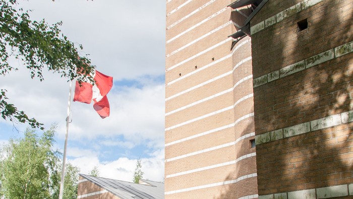 Et rødt flag på en stang foran et højt murstensbygning.