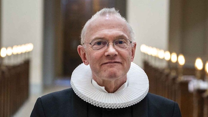 En mand med hvid krage og briller står i en kirke.