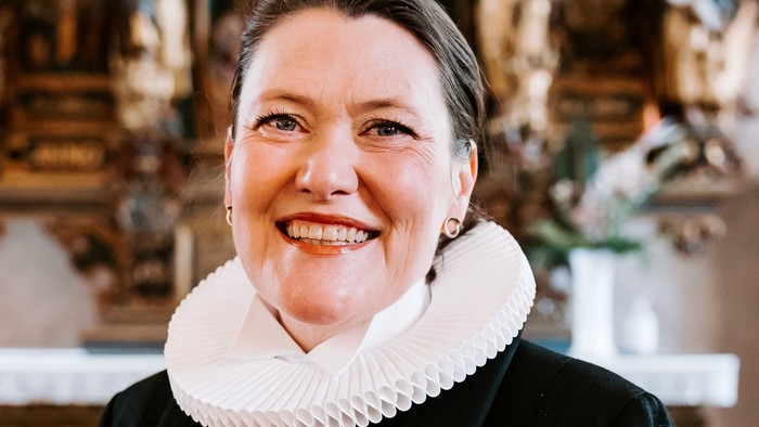 En kvinde i sort jakke med hvid krage står foran en prægtig altertavle.