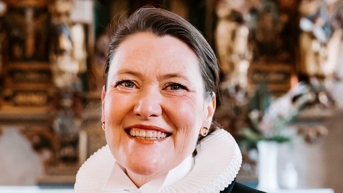 En kvinde i sort jakke med hvid krage står foran en prægtig altertavle.