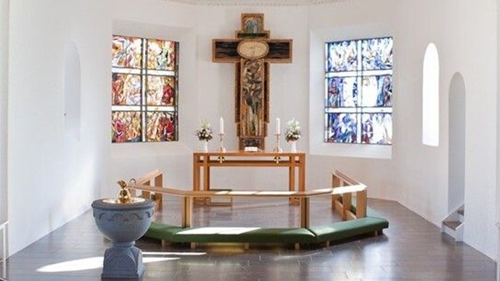 En lille kapel med alter, bænke og farverige vinduesglass.