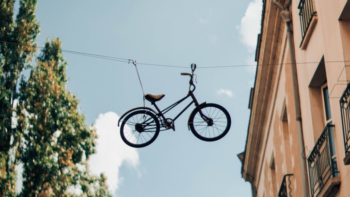 Ein Fahrrad schwebt zwischen zwei Gebäuden am klaren blauen Himmel.