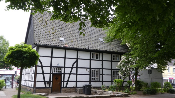 Das Bild zeigt ein traditionelles Fachwerkhaus mit einem steilen Dach und einem kleinen Vorgarten.