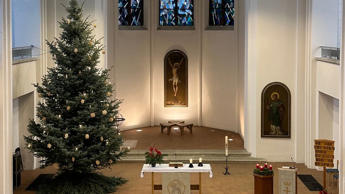 In der Kirche steht ein geschmückter Weihnachtsbaum vor dem Altar.