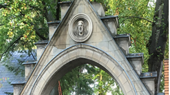 Steinbogen mit rundem Relief, umgeben von Grünpflanzen.