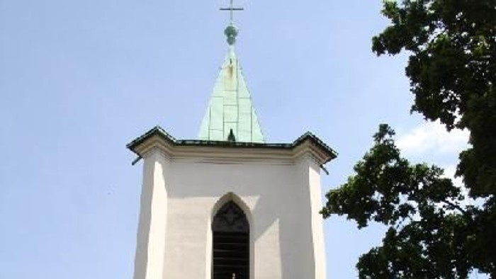 Kleine Kirche mit weißem Turm und grünem Dach, umgeben von Bäumen