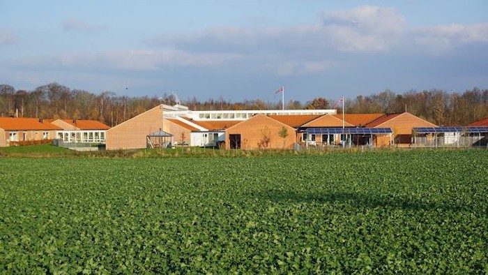En stor, orangefarvet bygning med blå tag i en grøn mark