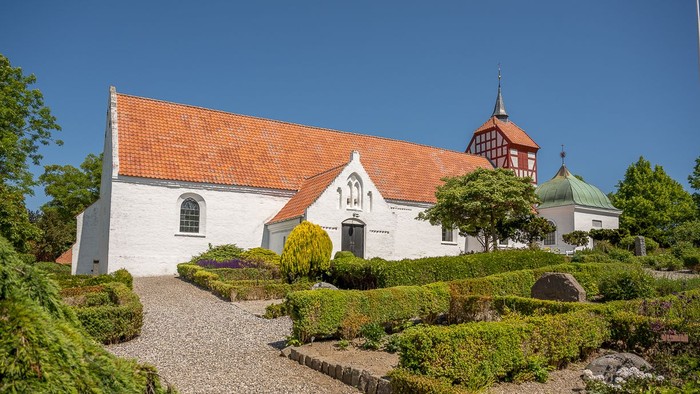 Hvid kirke med røde tag og smukke haver