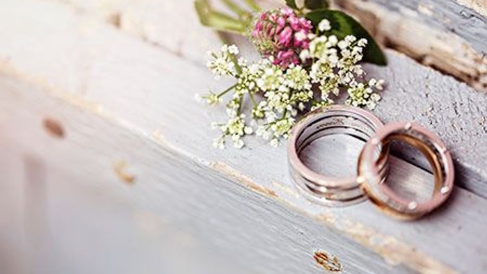 Zwei goldene Ringe und eine kleine Blumenanordnung auf einem Holzbalken