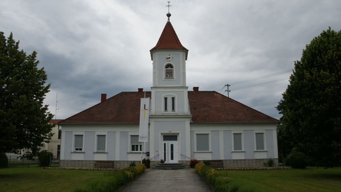 Eine charmante weiße Kirche mit rotem Turm und Uhr, eingebettet in eine grüne, gepflegte Landschaft.