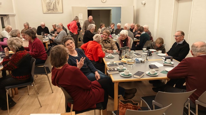 En gruppe ældre mennesker samlet omkring borde, der nyder en social begivenhed med te og samtale.