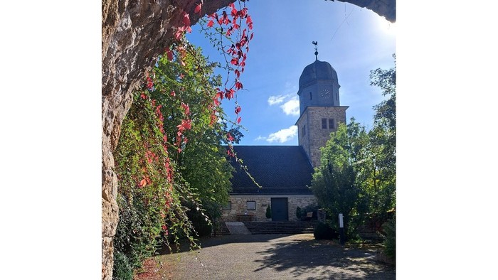 Kirche mit einem hohen Kirchturm und roten Blüten an einem Baum.