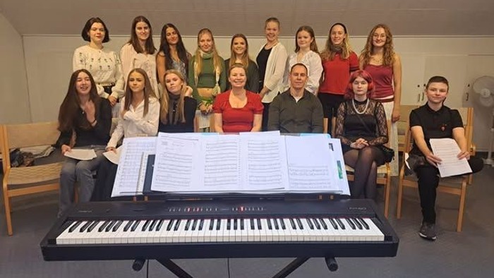 En gruppe musikere poser sammen med noder og et keyboard i et øvelokale.