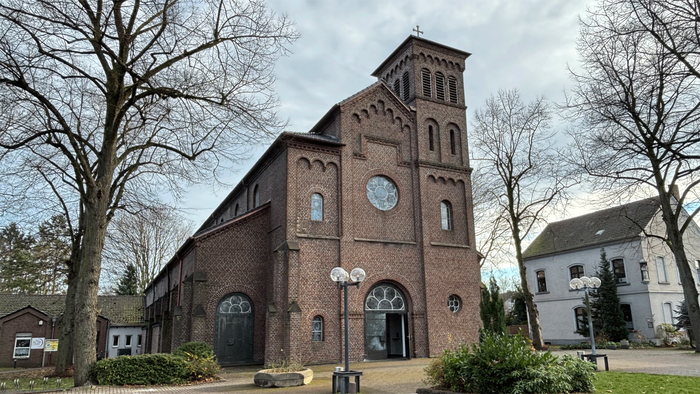 Ziegelsteinkirche mit Uhrturm und Bogenfenstern, umgeben von Bäumen und Straßenlaternen.