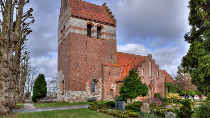 Historisk murstenskirke med et højt tårn og buede vinduer i en rolig, anlagt kirkegård.