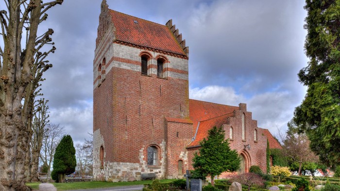 Historisk murstenskirke med et højt tårn og buede vinduer i en rolig, anlagt kirkegård.