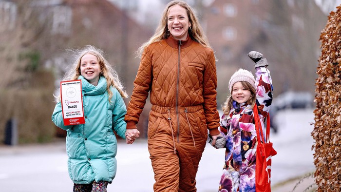 En kvinde og to børn går sammen udenfor, holder hinanden i hånden og smiler i vintertøj.