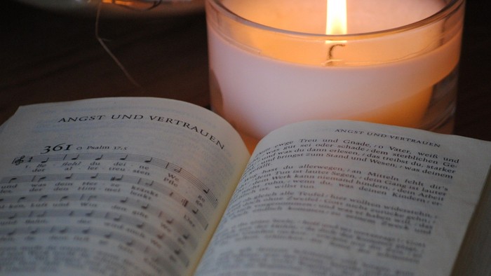 Öffne das Gesangbuch mit dem Titel *„Angst und Vertrauen“* und stelle eine brennende Kerze daneben, um eine ruhige Atmosphäre zu schaffen.